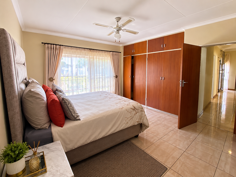 Spacious bedroom featuring tiled flooring, a ceiling fan, and extensive built-in wooden wardrobe storage.