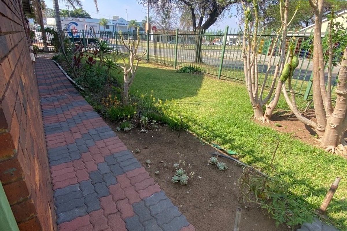 A side garden area featuring brick paving, a lawn, and metal perimeter fencing along the property boundary.