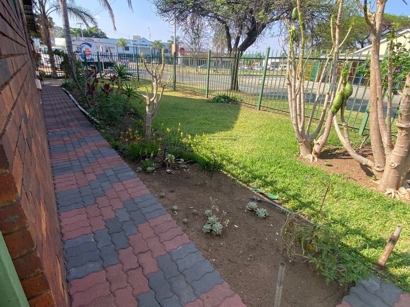 A side garden area featuring brick paving, a lawn, and metal perimeter fencing along the property boundary.