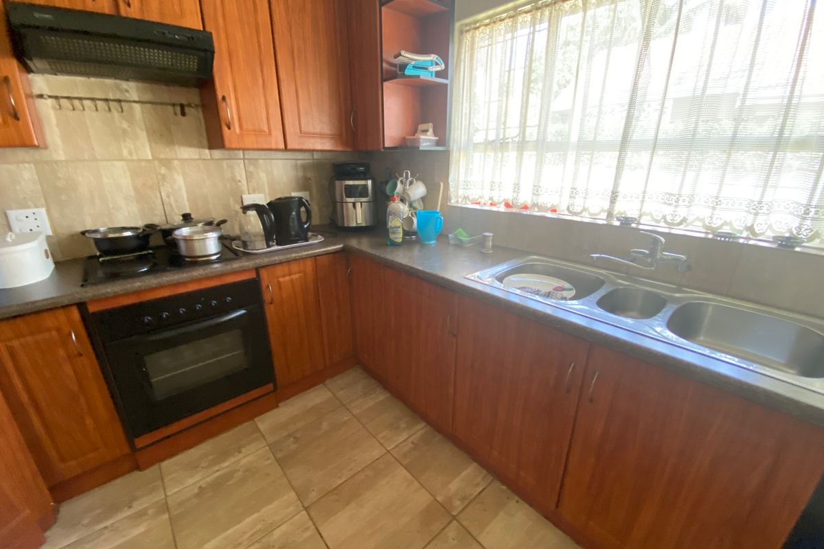 A functional kitchen featuring wooden cabinetry, laminate countertops, a built-in oven with hob, and a double bowl sink with tiled flooring and backsplash.
