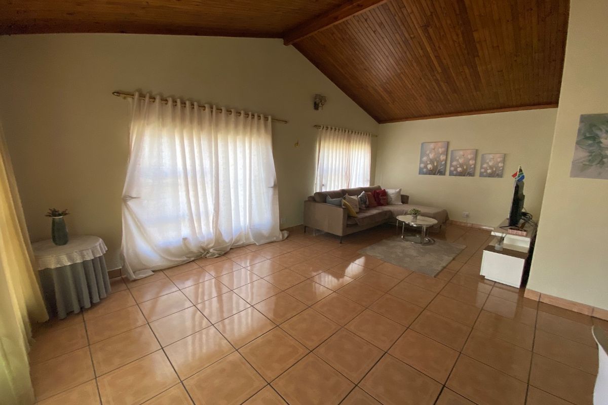 Spacious living room featuring a high vaulted timber ceiling and ceramic tiled flooring, offering a bright and open atmosphere.