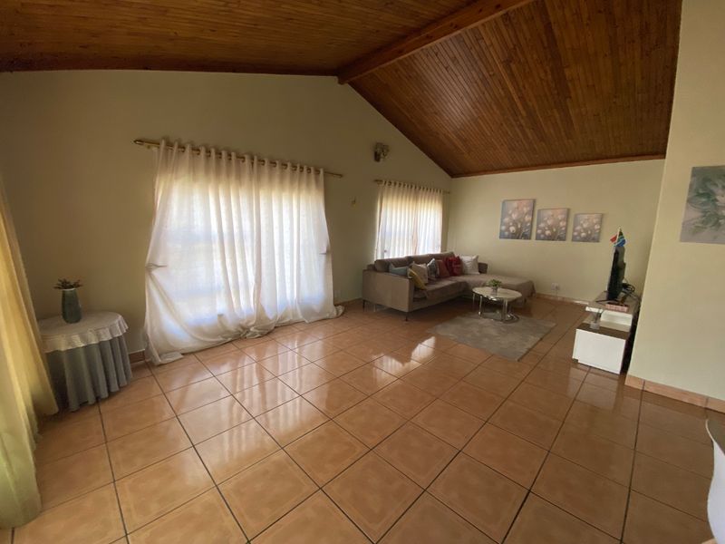 Spacious living room featuring a high vaulted timber ceiling and ceramic tiled flooring, offering a bright and open atmosphere.
