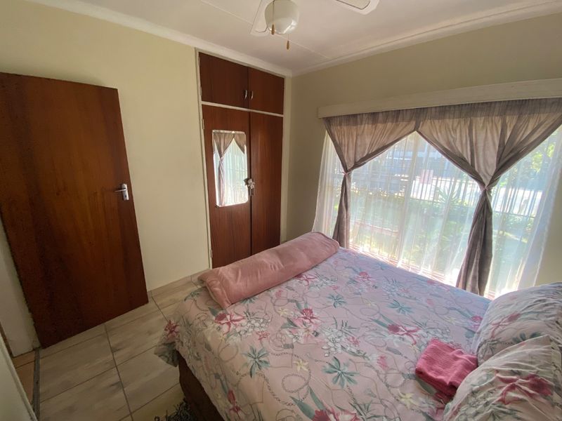 A functional bedroom featuring tiled flooring, a built-in wooden wardrobe, and a ceiling fan, offering a neutral base for potential interior updates.