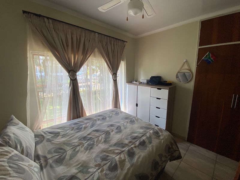 A functional bedroom featuring tiled flooring, a ceiling fan, and a built-in wooden cupboard, offering a comfortable and practical living space.