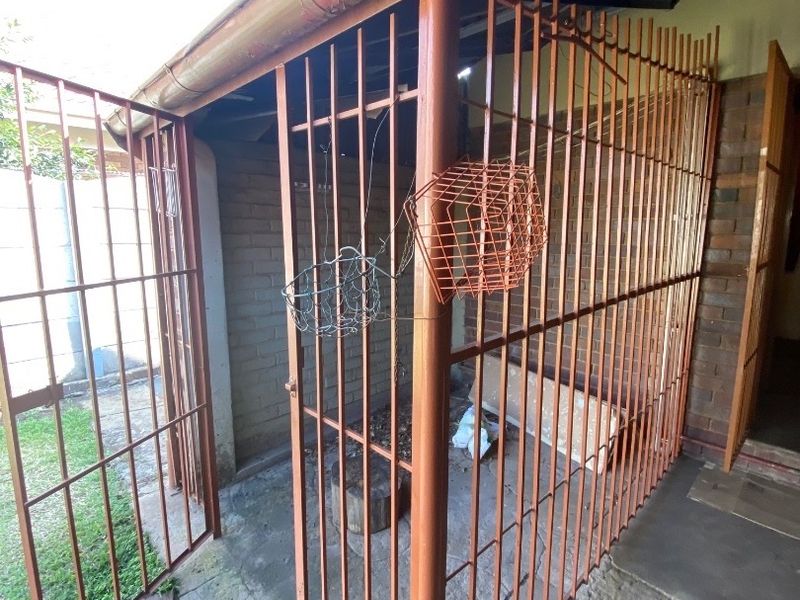 A secure, enclosed utility or storage area featuring metal security gates, brick walls, and concrete flooring, suitable for secure outdoor storage.