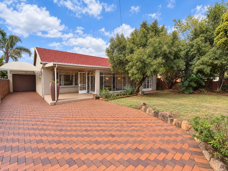 A well-maintained single-story home featuring a red tiled roof, a spacious brick-paved driveway, a carport, and a neat front garden with stone edging.