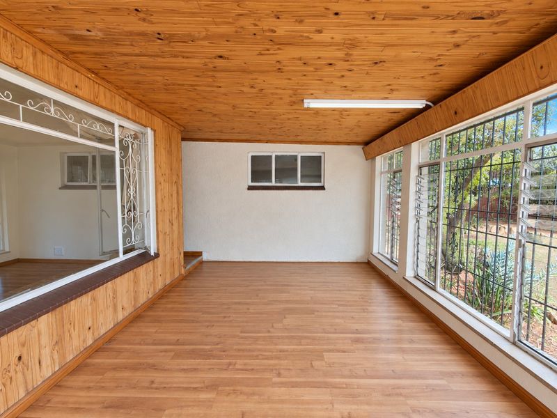 A bright, enclosed patio area featuring timber-clad ceilings, laminate flooring, and large windows with security bars, offering a versatile space for relaxation.