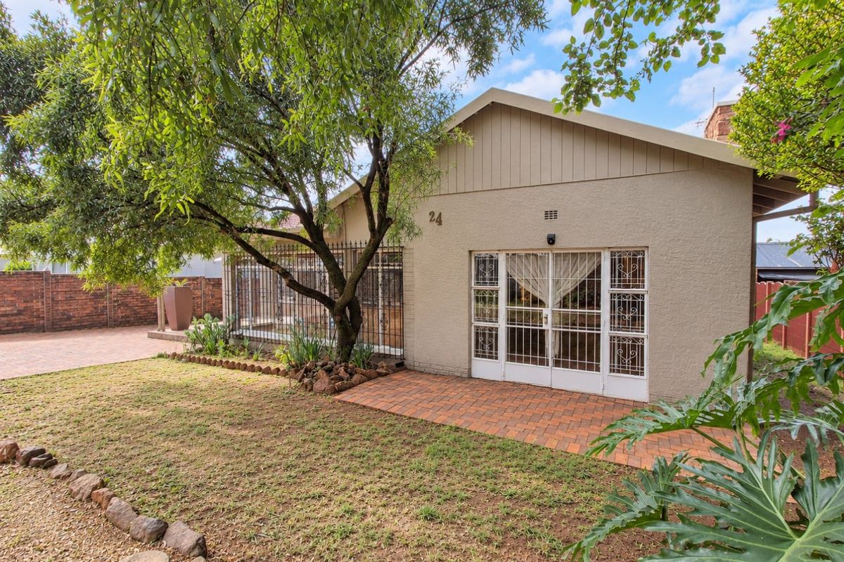 Rear view of the property featuring a paved patio area, established garden, and secure access points with security gates.