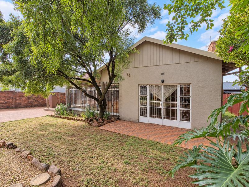 Rear view of the property featuring a paved patio area, established garden, and secure access points with security gates.