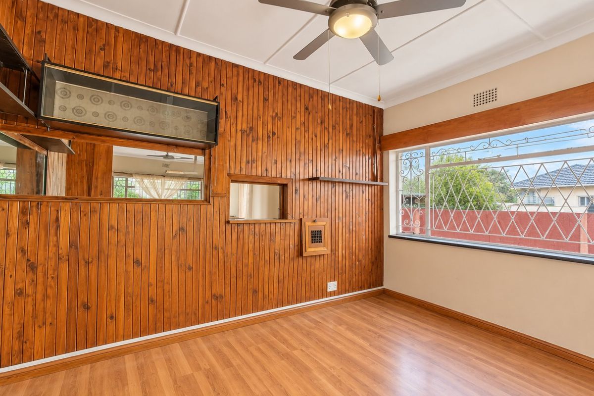 A vacant bedroom featuring timber wall paneling, laminate flooring, a ceiling fan, and security bars on the window.