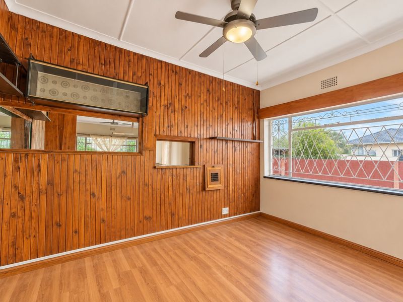 A vacant bedroom featuring timber wall paneling, laminate flooring, a ceiling fan, and security bars on the window.