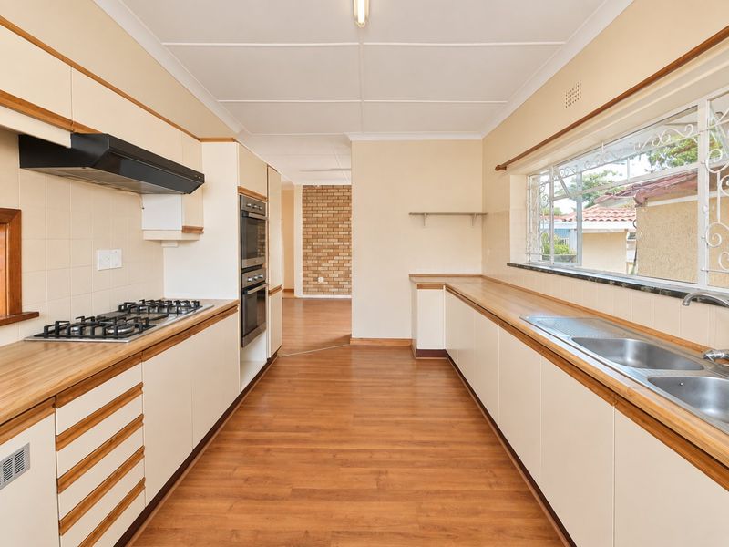 A functional galley-style kitchen featuring built-in cabinetry, a gas hob, double oven, and double stainless steel sink with laminate countertops.