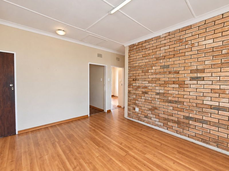 An empty living area featuring a prominent exposed brick feature wall, laminate flooring, and a neutral color palette, ready for personalization.