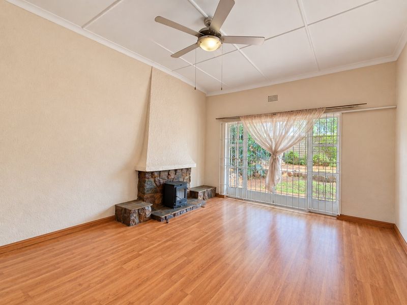 Spacious living room featuring laminate flooring, a stone fireplace with a wood-burning stove, and sliding glass doors leading to the garden.