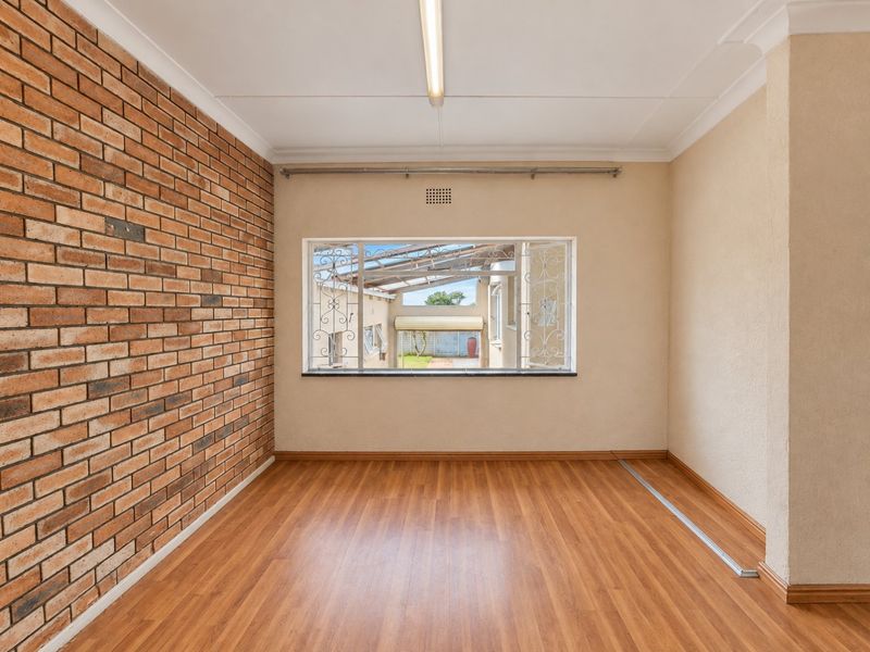 An empty living room featuring an exposed brick wall, laminate flooring, and a window with security bars, offering a neutral canvas for interior design.