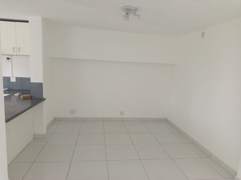 An empty open-plan living area featuring neutral tiled flooring and a partial view of the adjacent kitchen cabinetry and countertop.