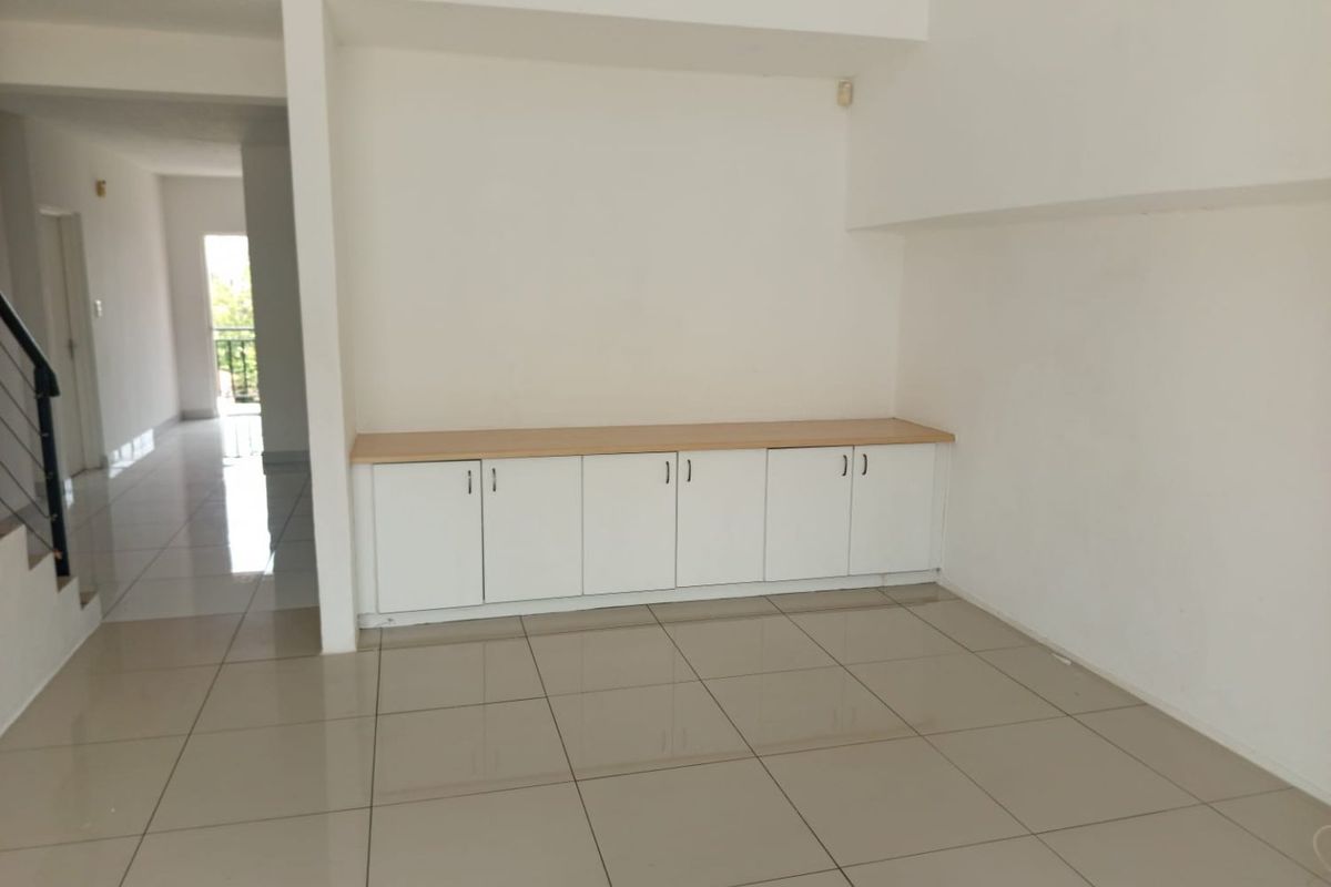 An empty living area featuring neutral tiled flooring and modern built-in cabinetry, offering a clean and versatile space for personalization.