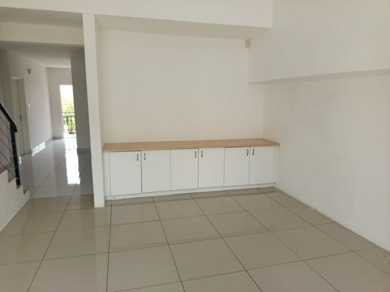 An empty living area featuring neutral tiled flooring and modern built-in cabinetry, offering a clean and versatile space for personalization.