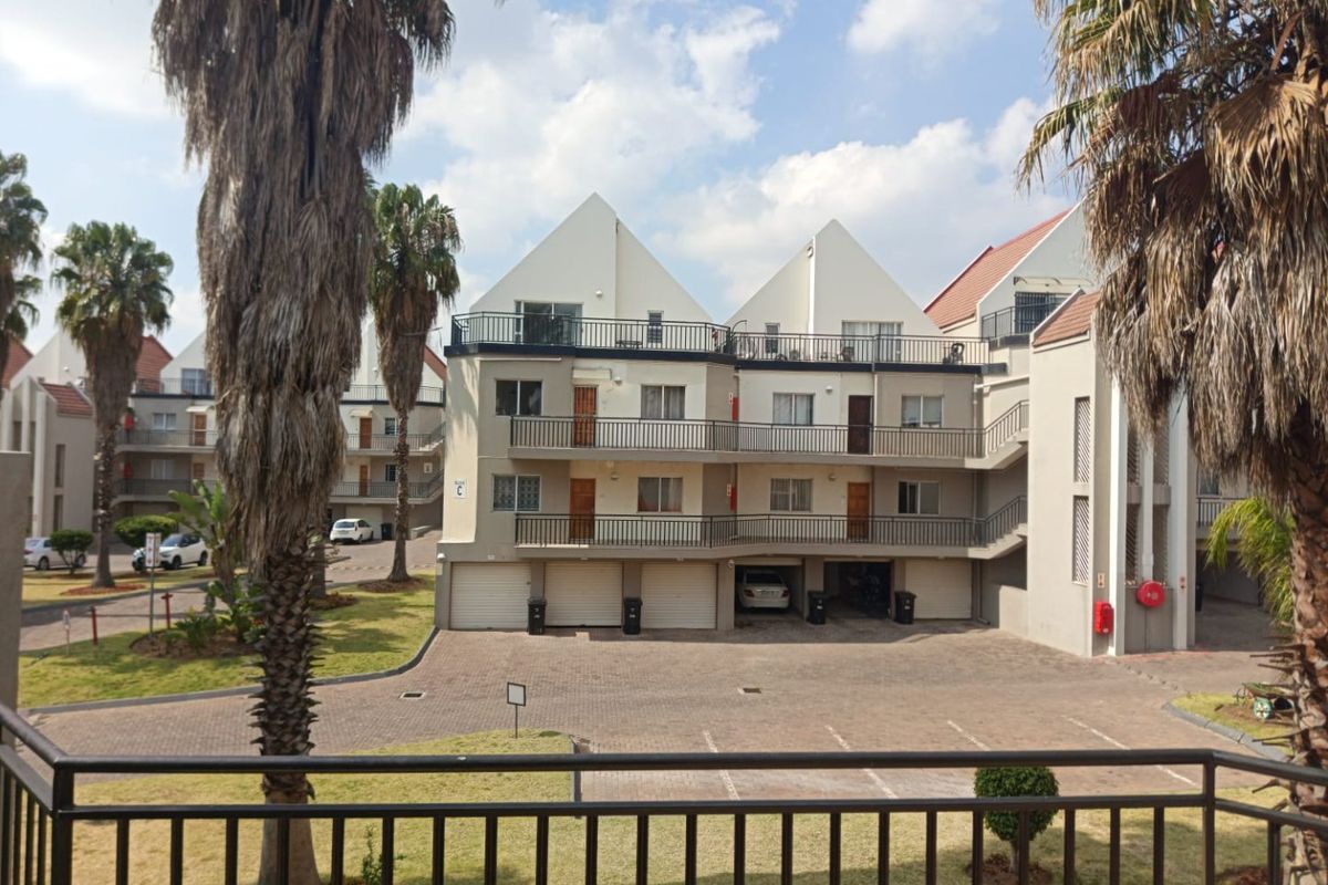 Exterior view of a multi-story townhouse complex featuring paved parking, garage access, and private balconies with metal railings.