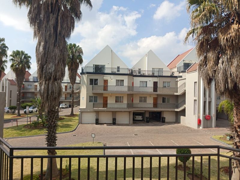 Exterior view of a multi-story townhouse complex featuring paved parking, garage access, and private balconies with metal railings.