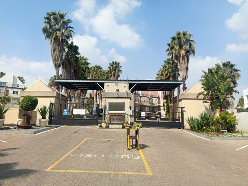 Front entrance view of the townhouse complex featuring a secure gated access point, guard house, and paved visitor parking area.