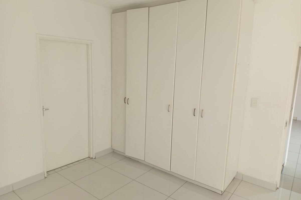A clean, empty bedroom featuring white built-in cupboards and neutral tiled flooring, offering a blank canvas for personalization.