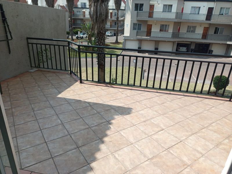 An open-air balcony featuring tiled flooring and a black metal balustrade, overlooking the complex grounds and parking area.