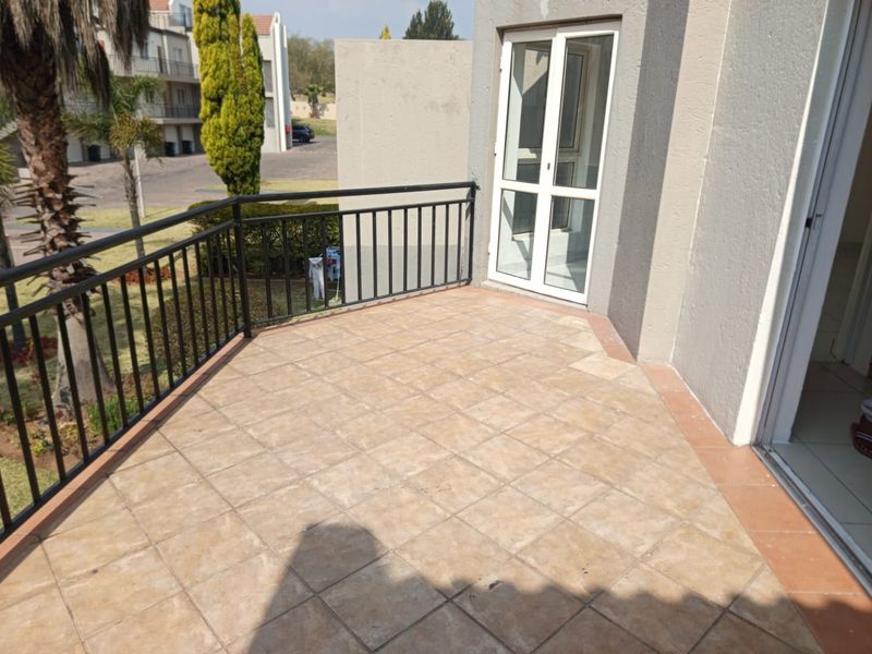 A spacious outdoor balcony featuring tiled flooring and a secure metal balustrade, providing an open-air space accessible through glass doors.