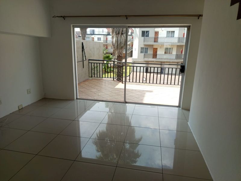 An empty, well-lit living area featuring large format floor tiles and a sliding glass door leading to an outdoor patio space.