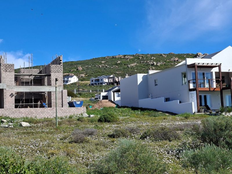 View of a residential property under construction featuring concrete block walls and scaffolding alongside an existing finished home in a coastal setting.