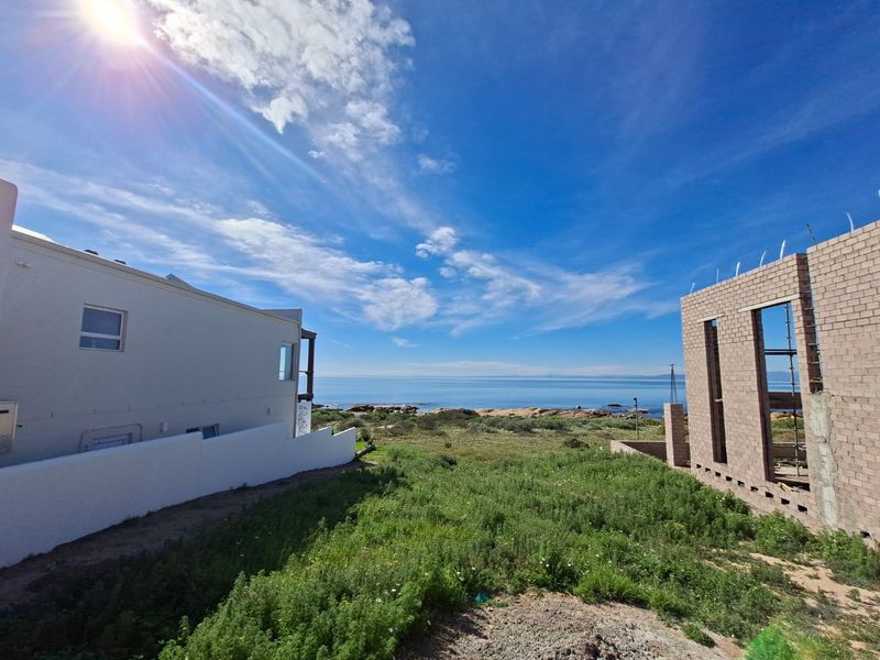 A scenic view of the coastline and ocean from a residential plot, featuring adjacent building structures and natural vegetation.