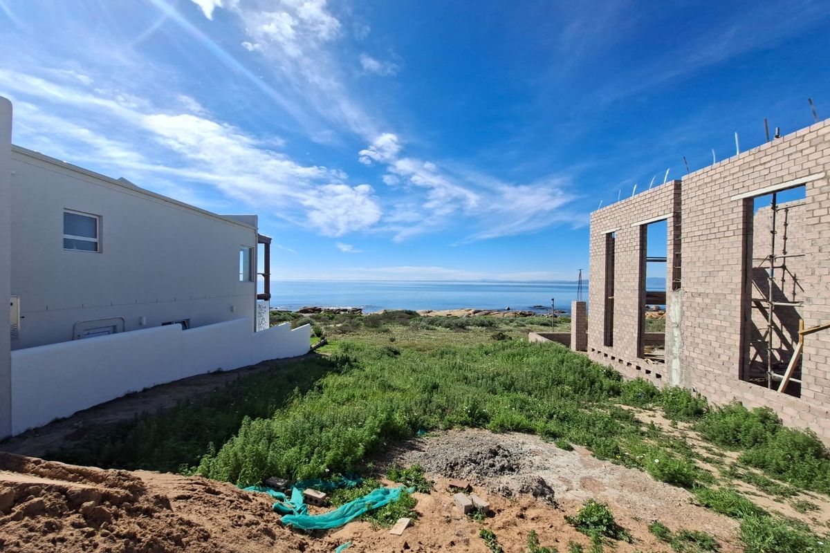 A view of a residential construction site featuring an unfinished brick structure adjacent to an existing home with ocean views.