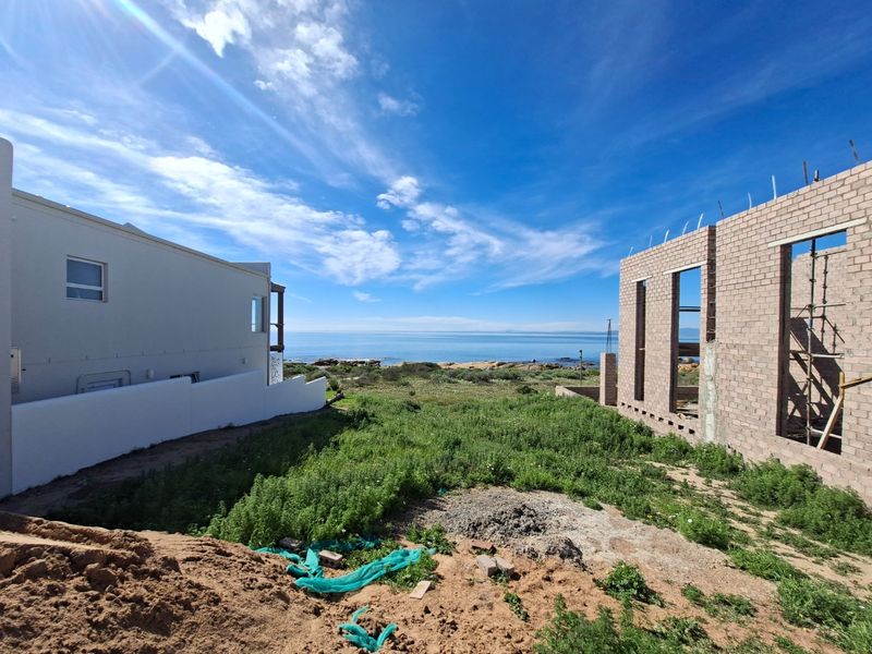 A view of a residential construction site featuring an unfinished brick structure adjacent to an existing home with ocean views.