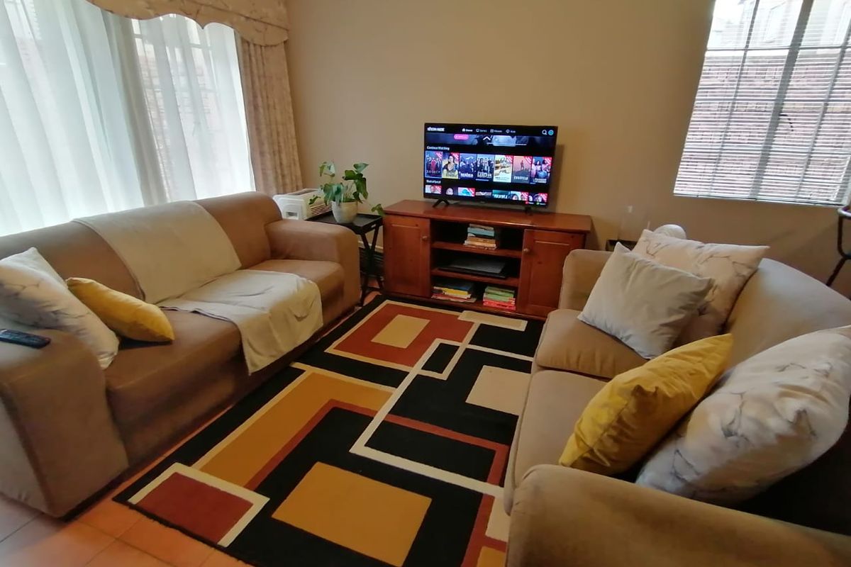 A comfortable living room featuring tiled flooring, window blinds, and a curtain pelmet, providing a functional space for relaxation.