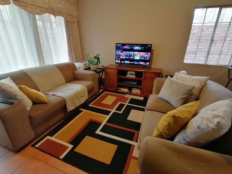 A comfortable living room featuring tiled flooring, window blinds, and a curtain pelmet, providing a functional space for relaxation.