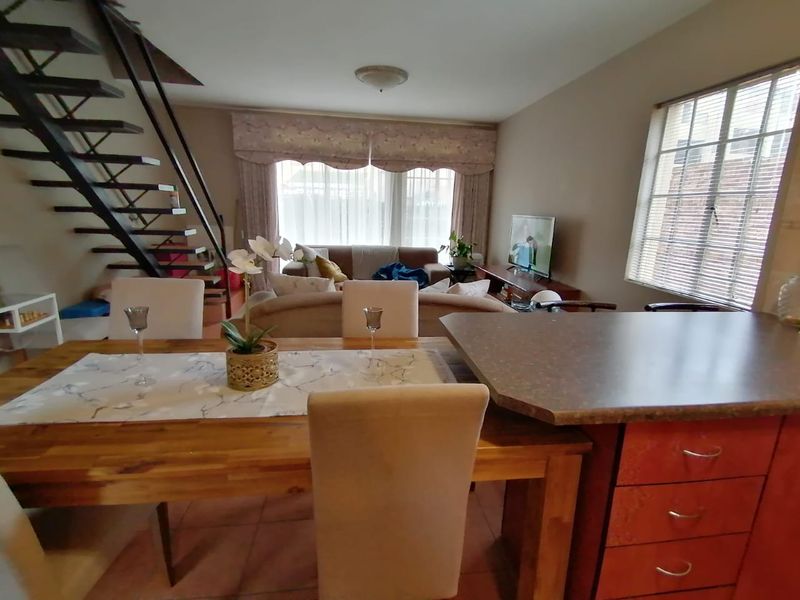 Open plan living and dining area featuring a staircase, tiled flooring, and kitchen cabinetry with a breakfast counter.