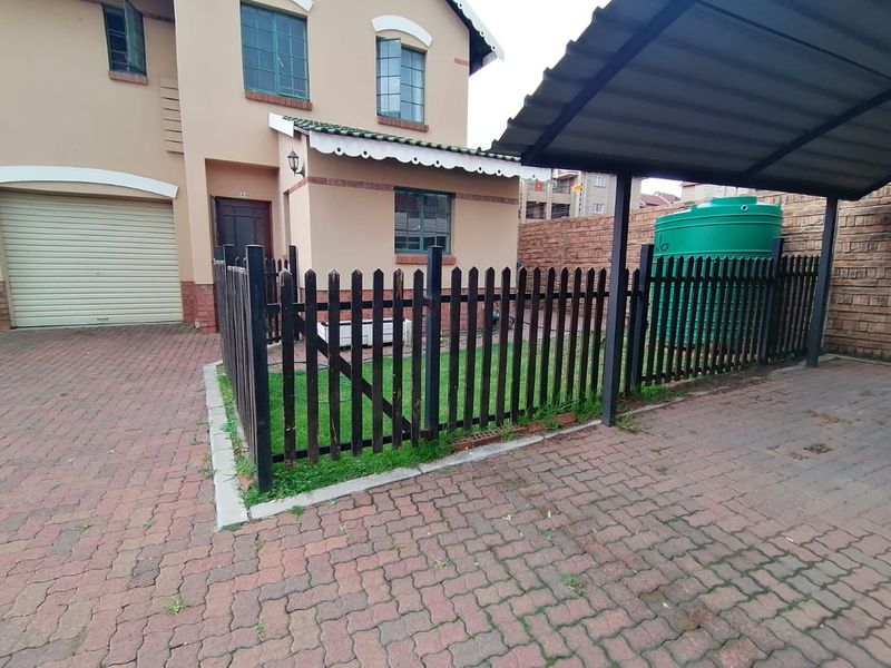 Front exterior view of the property featuring a paved driveway, covered carport, enclosed garden area with picket fencing, and a water storage tank.