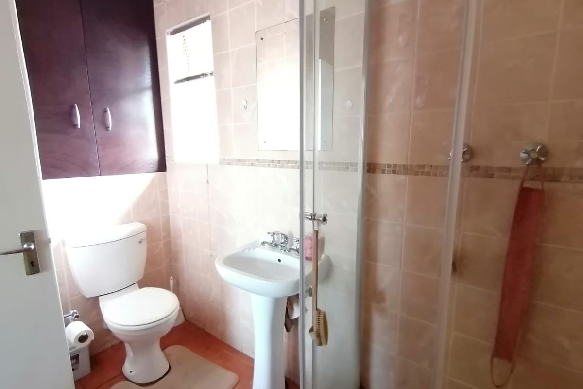 A functional bathroom featuring a pedestal basin, toilet, and a glass-enclosed shower with tiled wall finishes and built-in storage cabinetry.