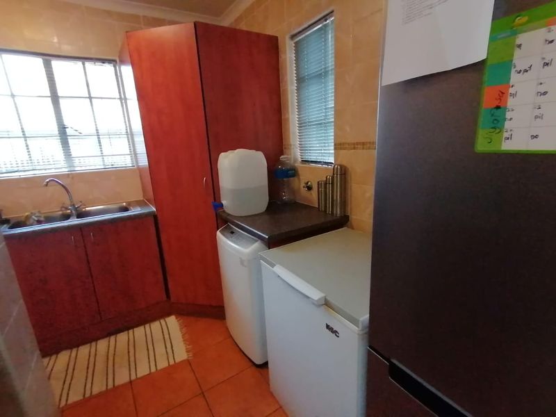 A functional scullery area featuring tiled walls, laminate cabinetry, and a double basin sink with natural light from the window.