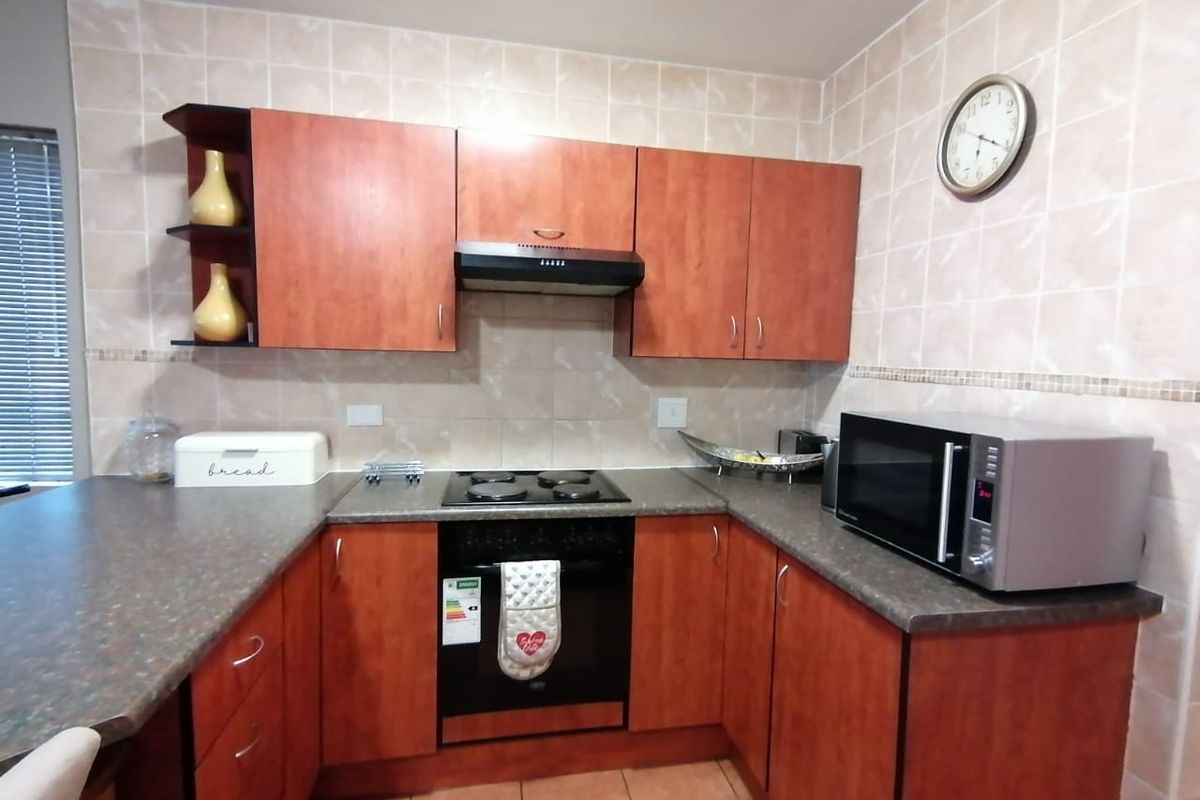 A functional kitchen featuring wood-look cabinetry, laminate countertops, tiled splashbacks, and integrated cooking appliances including an oven, hob, and extractor fan.