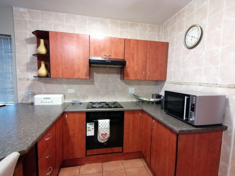 A functional kitchen featuring wood-look cabinetry, laminate countertops, tiled splashbacks, and integrated cooking appliances including an oven, hob, and extractor fan.