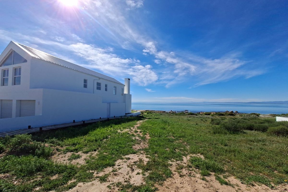 A rear view of a modern white coastal residence featuring a metal roof, chimney, and a timber boardwalk leading toward the ocean.