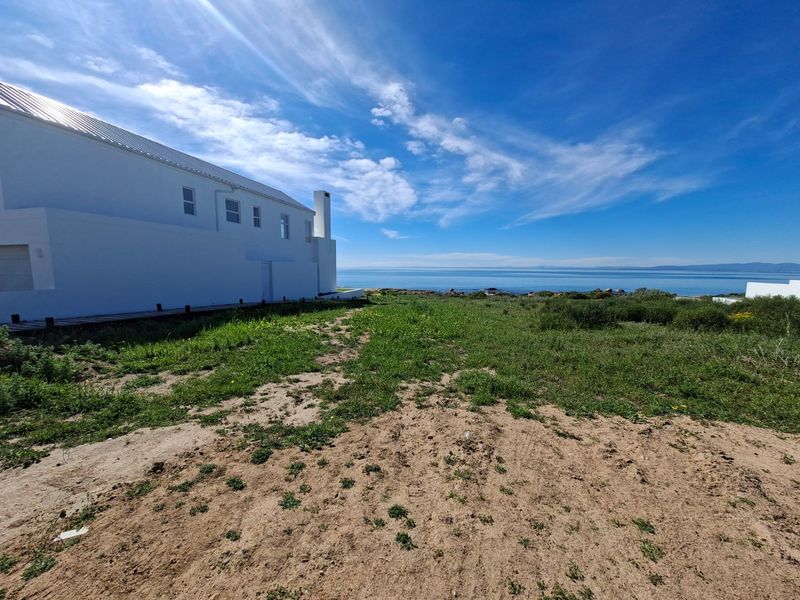 Rear view of a white coastal property featuring a metal roof, external chimney, and wooden decking overlooking the ocean.