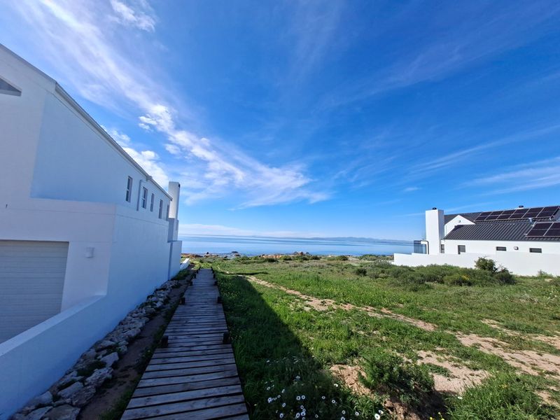 A scenic view of the coastline featuring a wooden boardwalk leading towards the ocean, flanked by modern residential properties.