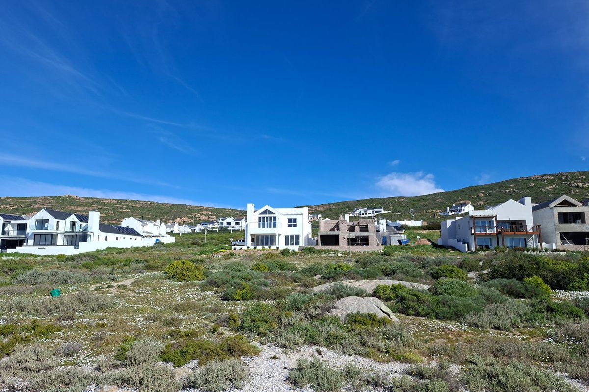 An aerial view of a coastal residential area featuring established homes and ongoing construction projects set against a natural hillside landscape.