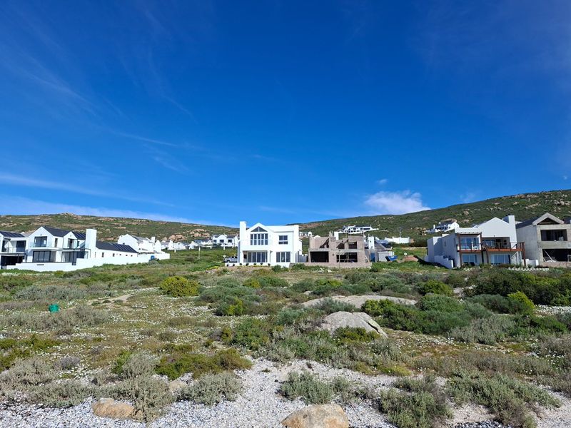 An aerial view of a coastal residential area featuring established homes and ongoing construction projects set against a natural hillside landscape.