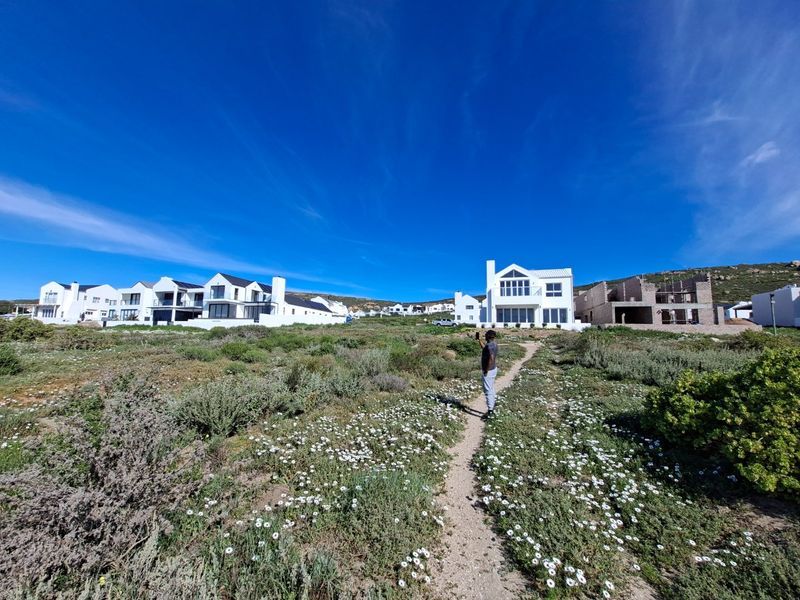 A wide-angle view of a coastal residential estate featuring established modern homes and vacant plots with natural fynbos vegetation.