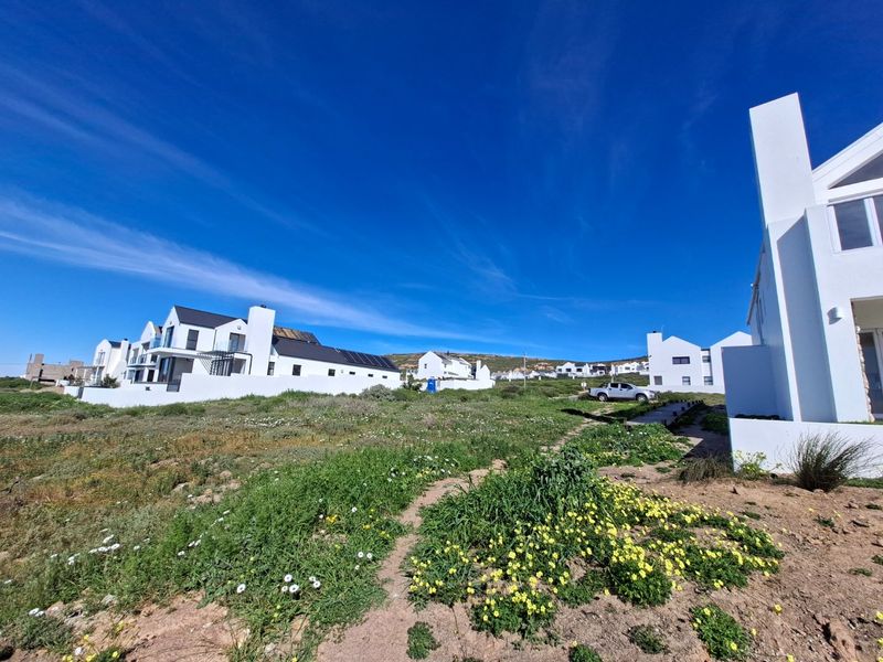 A view of the rear exterior of modern white residential properties with solar panels, set within a natural coastal landscape.