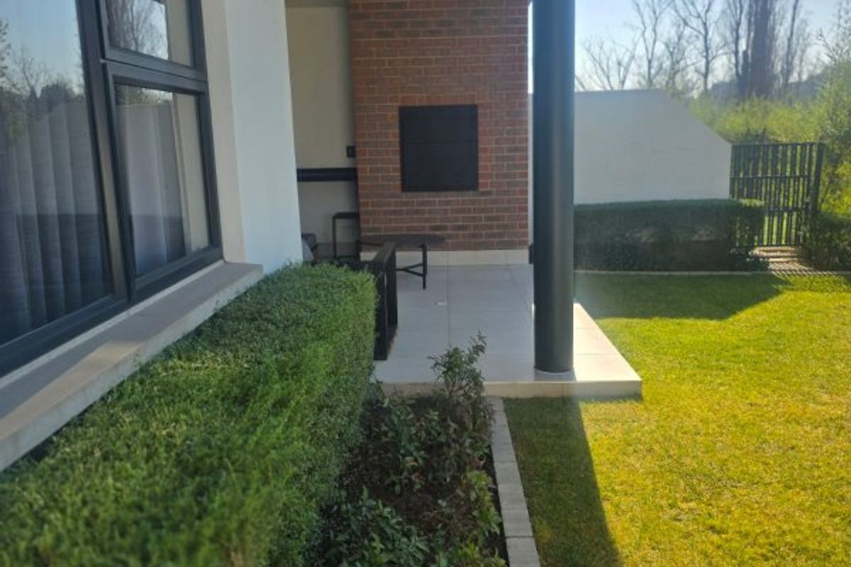 A covered patio area featuring a built-in braai, brick accent wall, and tiled flooring, overlooking a private garden space.