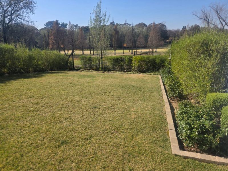 A well-maintained private garden featuring a manicured lawn, neat brick edging, and established perimeter hedges with views of the surrounding landscape.